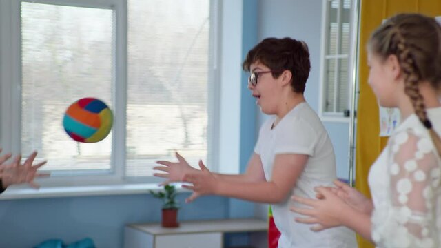 male child with disabilities has fun playing ball in an inclusive classroom during therapy for children with down syndrome