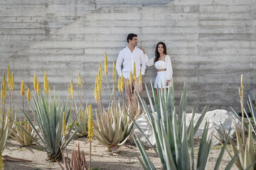 Couple dress in white next to a grey wall and flowers