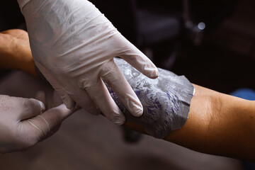A tattoo artist copies a drawing on the arm of a customer