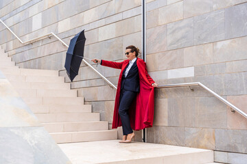 Obraz na płótnie Canvas business woman dressed in red coat and suit holding an umbrella on modern design staircase on the street