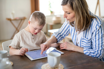 Single mother with down syndrome son with tablet at home, distance learning.