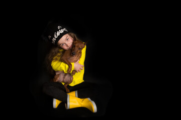 A cute little toddler girl hugs her dog, the Miniature Pinscher. Studio shooting on a black background. 