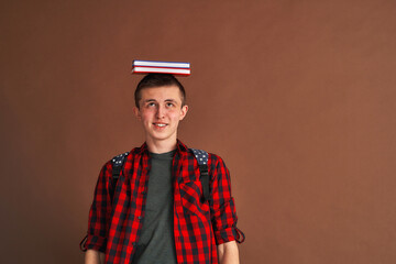 surprised, joyful teenage student in casual clothes with a backpack, holding books on his head, isolated against a brown background. Higher school education, the concept of a university college.