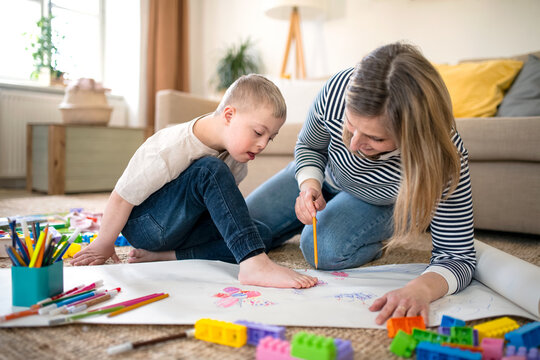 Single mother with down syndrome child at home, drawing pictures.