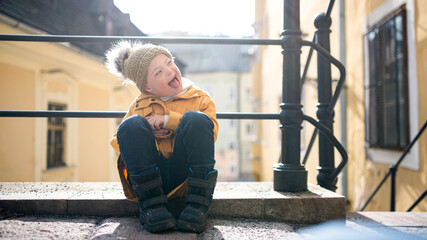 Portrait of down syndrome child outdoors in town, making faces. - obrazy, fototapety, plakaty