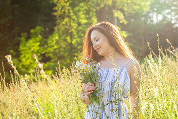 Naklejka na ściany i meble Young woman walking among wildflowers on sunny summer day. Concept of the joy of communicating with summer nature