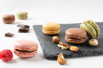 Variety of french macaroons with raspberry, nuts and chocolate on white wooden table.