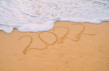 Closeup image of sea waves washing 2022 new year numbers from sand on the beach. Concept of New Year, Christmas and travel on winter holidays.