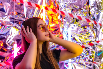 beautiful young girl listening to music in neon light. portrait of a girl, a DJ in headphones in the style of cyberpunk in the light of the night party