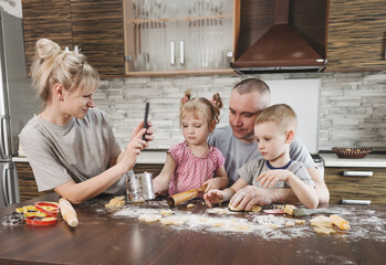 happy mom takes pictures of dad with two young children in the kitchen while making flour cookies. happy family cooking together