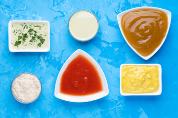 Different type of sauces in different white bowls on blue cement background