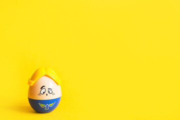 Funny egg toy with a man's sad face on a yellow background. Easter, solitude. Copy space