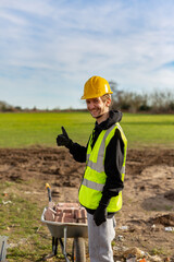 A young adult male builder wearing a high visibility vest and hard hat while giving a thumbs up