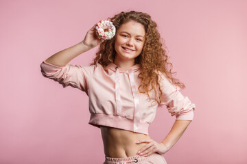 Young beautiful girl with curly hair holds a pink donut with marshmallows. Pink background.