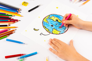 Child girl draws planet earth with multicolored felt-tip pens on a white sheet.