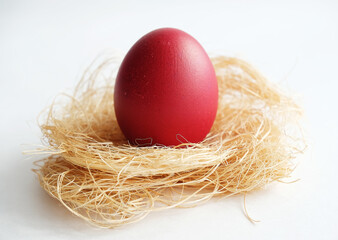 Red Easter dyed egg on coconut fiber on a white background close up