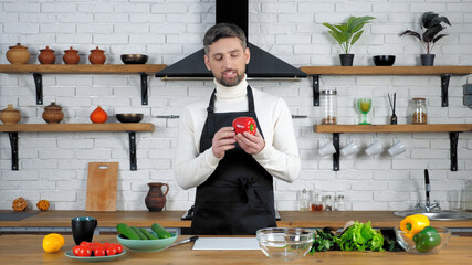 Man chef food blogger in black apron looking red bell pepper tells records remote online video...