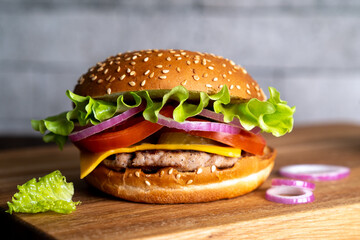 hamburger with cutlet, tomato, cheese and lettuce leaves on a wooden board