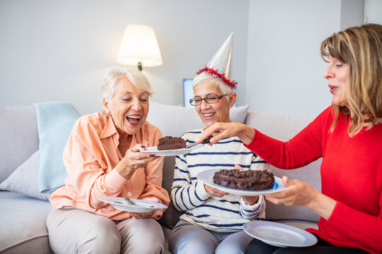 Close-up Of Happy, Excited Pensioners During A Birthday Party. Active Seniors Concept. Senior Woman Blows Out Birthday Cake Candles At Family Party. Seniors Celebrating A Birthday In A Retirement Home