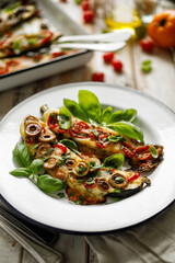 Zucchini stuffed with cheese and vegetables on an enameled white plate, close-up view