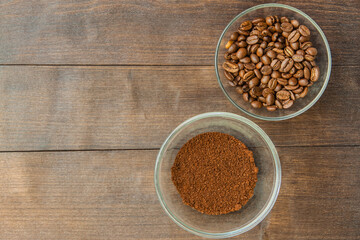 Coffee beans and grounded coffe in the bowls laying on the wooden background