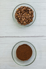 Coffee beans and grounded coffee in the glass bowls on the wooden background