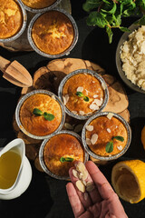 Delicious freshly baked lemon muffins sprinkled with almond flakes, top view. Homemade magdalena on a dark wooden table. Baking preparation idea, cupcake layout, vertical frame