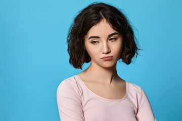 Obraz premium upset curly young brunette woman on blue background.