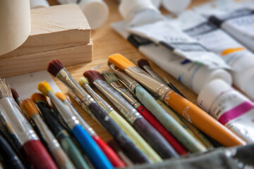 Paintbrushes, blur tempera tubes on wooden table background.