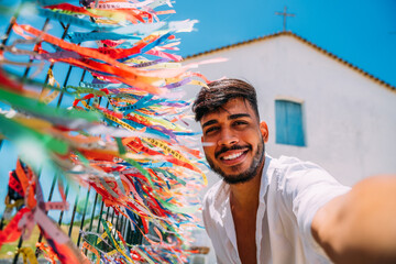 Smiling friendly young latin american man taking a selfie with the colorful ribbons of our lord of Bonfim. - obrazy, fototapety, plakaty