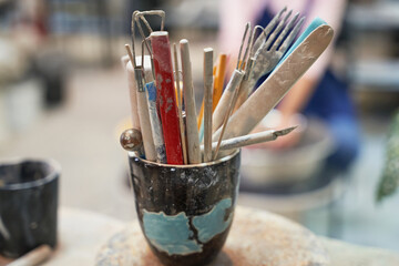 Pottery. Close up shot of jar with tools, brushes for creating handmade clay ceramics in workshop studio