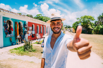Tourist making selfie in the historic center of Porto Seguro. Latin American man in hat and thumb...