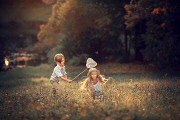 Beautiful girl and boy are catching butterflies with their butterfly net in summer park. Image with...