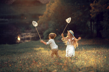 Beautiful girl and boy are catching butterflies with their butterfly net in summer park. Image with selective focus and toning