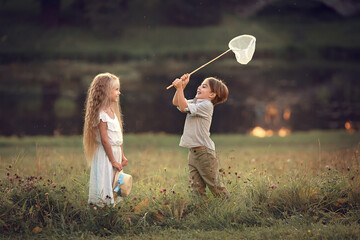 Cute little boy and beautiful long-haired girl are catching butterflies  with the butterfly net. Image with selective focus and toning