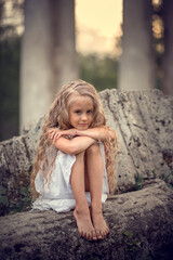 Portrait of beautiful blonde long-haired girl sitting on the ruined stones during the sunset in Pavlovsk park, Russia. Image with selective focus and toning