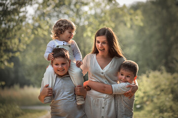 Fototapeta na wymiar Family portrait with young beautiful mother with her three sons in a park. Mother's face expression is very funny. Image with selective focus and toning