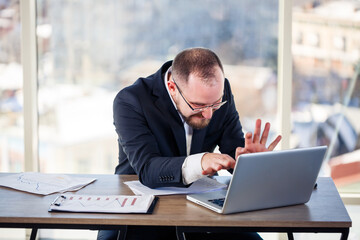 The corporate madman is sitting at the computer in the office and going crazy, the emotional portrait of the man at the table. Crazy worker at his workplace