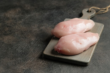 Chicken fillet on a cutting board on a dark background with copy space.