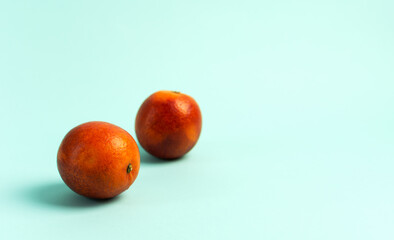 Two ripe red oranges on a blue background.
