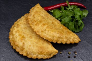 Chebureks on a black background. Served with coriander and red chili pepper. Caucasian cuisine.