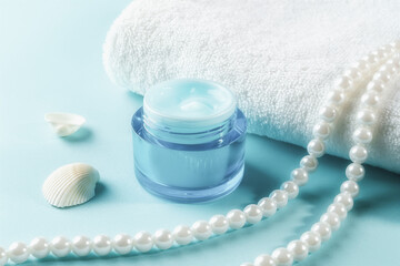 Jar of moisturizing facial gel and pearl beeds near white towel over blue wooden surface. Blue...