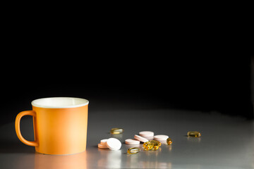 Orange ceramic mug on a gray table on a black background with omega-3 capsules and effervescent tablets with vitamins. Food supplements, vitamins, Omega-3. Health care, immunity support.