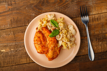 Baked chicken breast in sauce with salad on a plate next to a fork on a wooden table.
