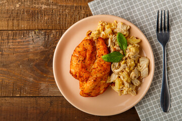 Baked chicken breast on a beige plate with pineapple salad on the table on a napkin next to a fork
