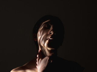 Female abuse. Domestic violence. Social pressure. Art portrait of suffering victim woman silhouette with hands on throat abstract shadow pattern on face isolated on dark night copy space background.