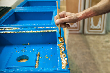 the master uses a brush to cover the wooden billet with gold leaf. Furniture manufacturing - obrazy, fototapety, plakaty