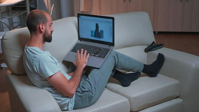Tired arhitect man working at industrial cad prototype while sitting on sofa. Caucasian male looking at laptop computer display for new technical construction concept late at night in kitchen