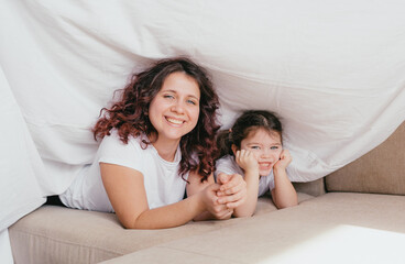 a happy little girl in a light turtleneck hugs her mother under a white sheet. a loving and caring mother