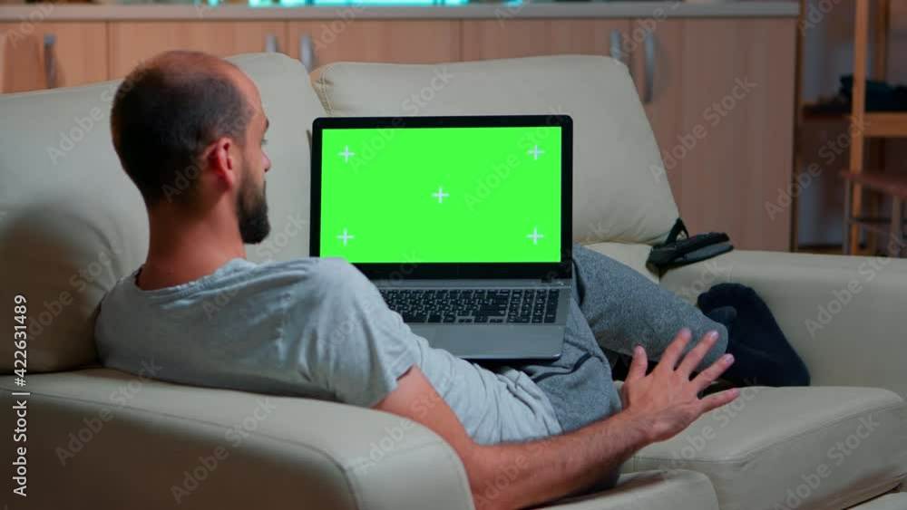 Poster focused man looking laptop computer with at mock up green screen chroma key display while laying on 